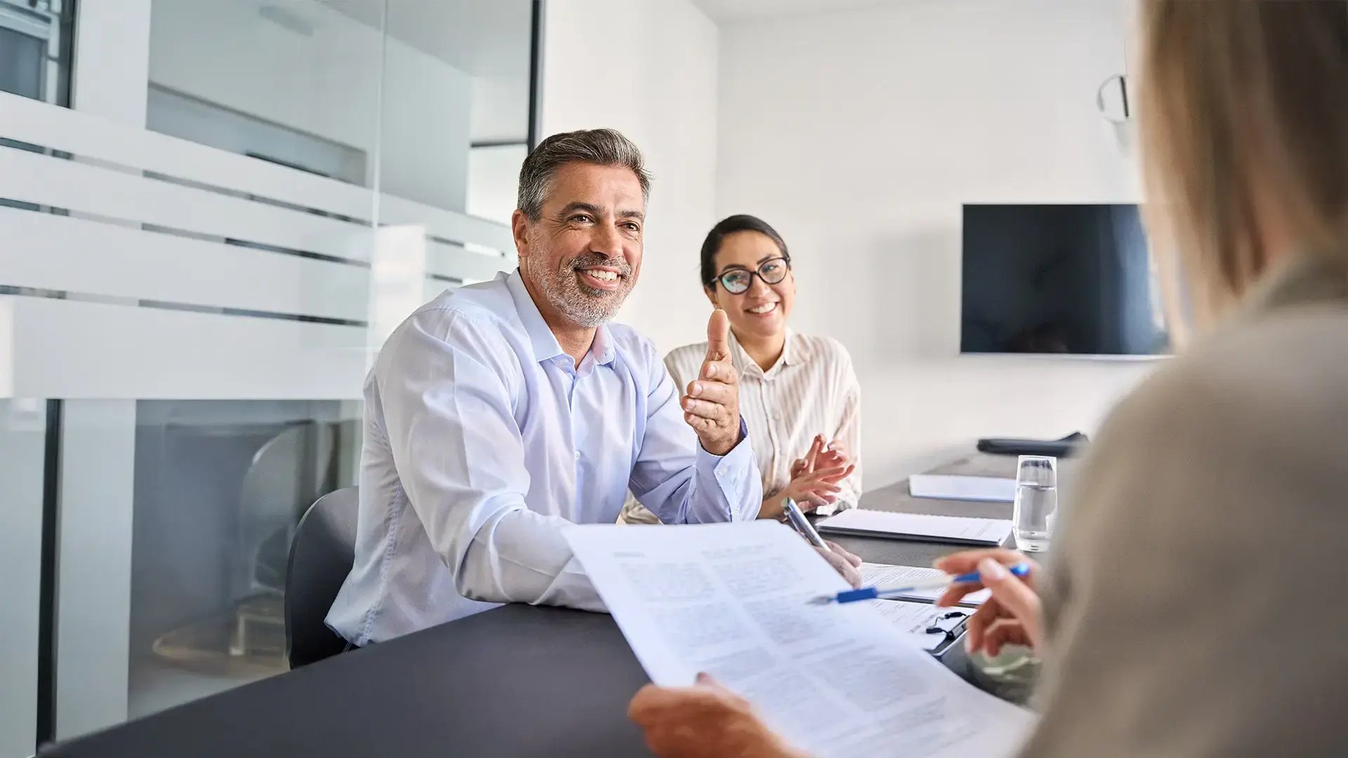 Persona mayor sonriente conversando con asesores legales sobre la renegociación de sus deudas.