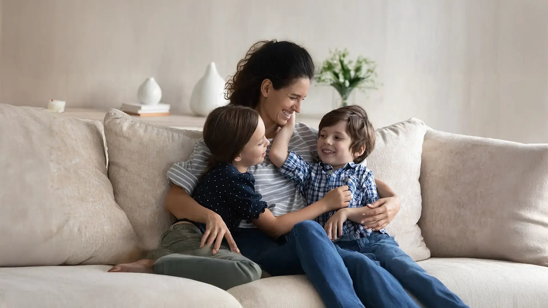 Madre compartiendo un momento afectuoso con sus dos hijos en un sillón.