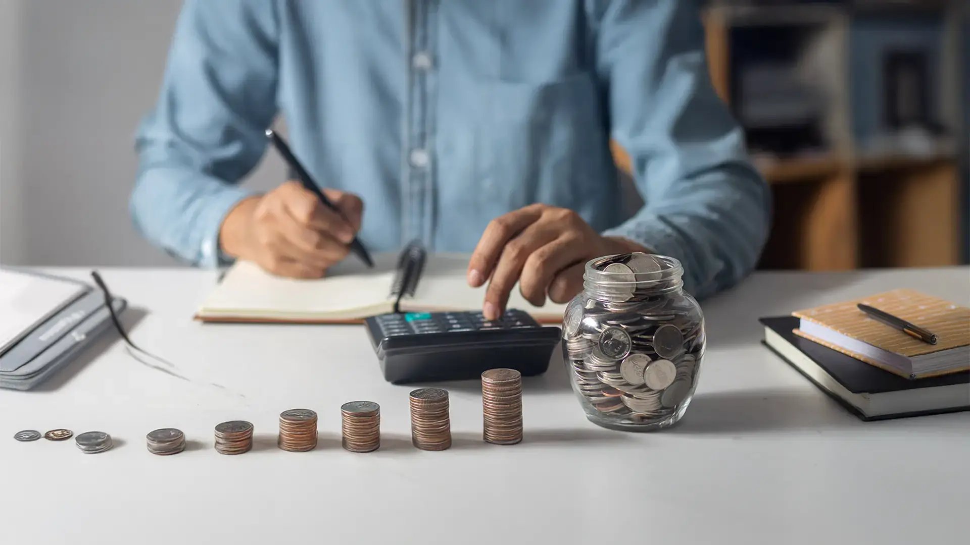 Persona realizando cálculos financieros con monedas y calculadora para determinar el pago de la pensión de alimentos.
