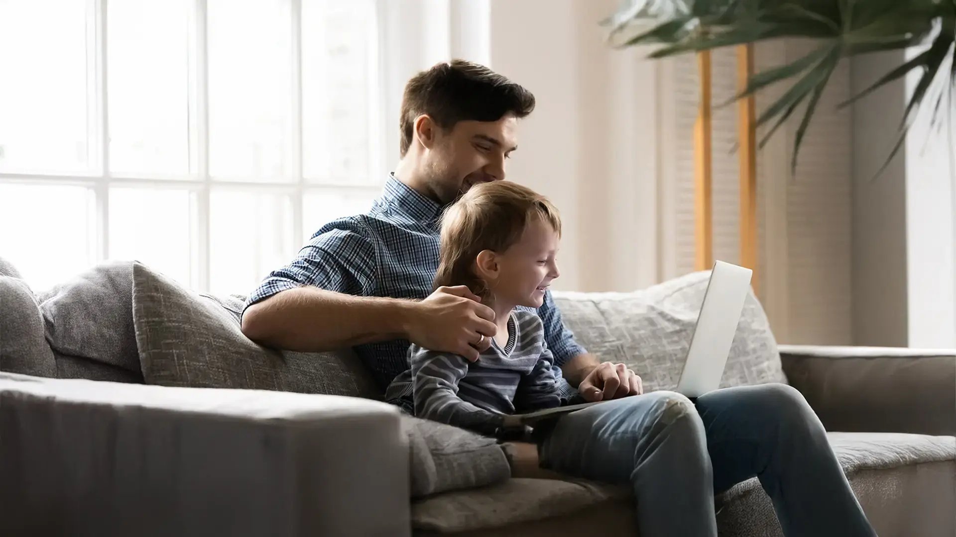 Padre e hijo sentados en el sofá frente a un computador.